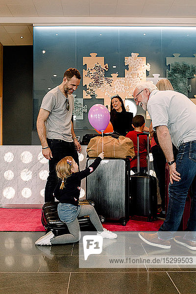 Eltern betrachten Mädchen mit Ballon in der Hand  während sie im Hotel auf einem Koffer sitzen