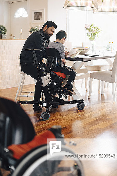 Side view of father teaching autistic son while sitting at table in living room