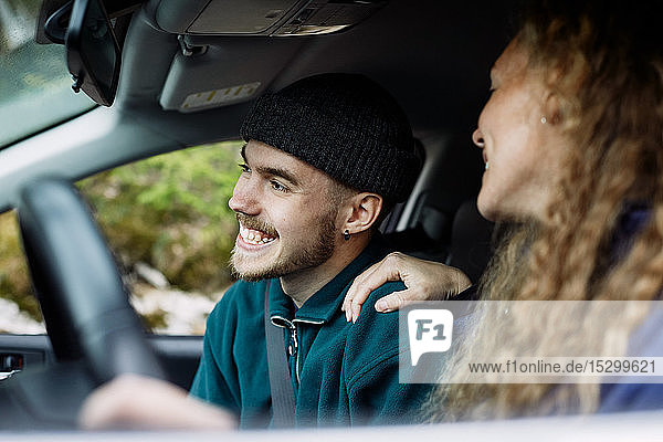 Junge Frau im Gespräch mit lächelndem männlichen Freund beim Autofahren