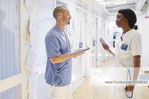 Multiethnische Beschäftigte im Gesundheitswesen diskutieren stehend im beleuchteten Korridor des Krankenhauses