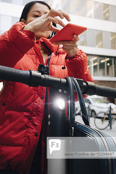 Female commuter scanning QR code on electric push scooter handlebar with smart phone