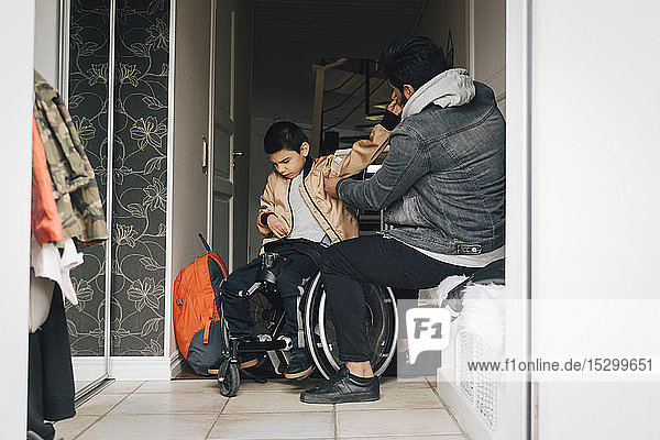 Father assisting disabled son in getting dressed at doorway