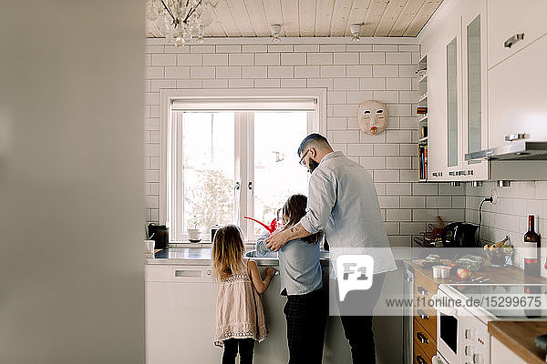 Mann steht mit Mädchen  während er der Tochter an der Küchenspüle assistiert