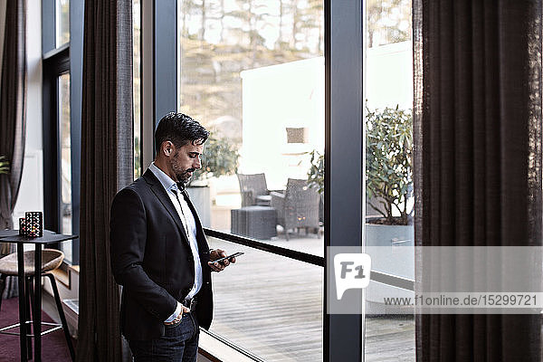 Businessman using phone while standing by window in office