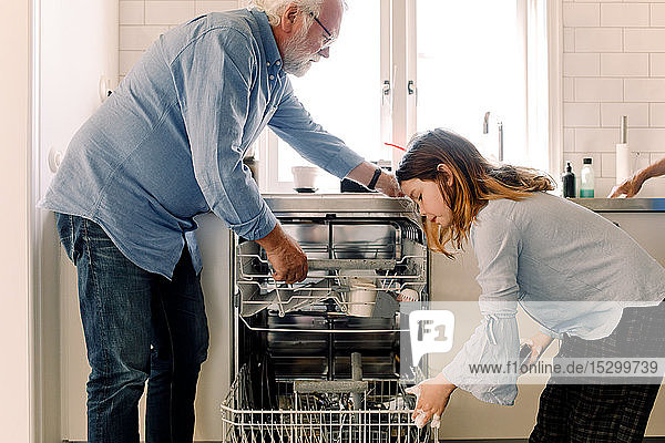 Großvater hilft Enkelin bei der Reinigung des Geschirrspülers in der Küche