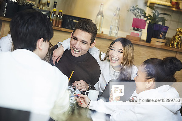 Freundinnen und Freunde lächeln  während sie in einem Café am Tisch sitzen