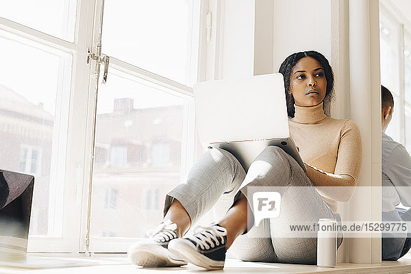 Computerprogrammiererin in voller Länge schaut weg  während sie im Büro am Fenster sitzt
