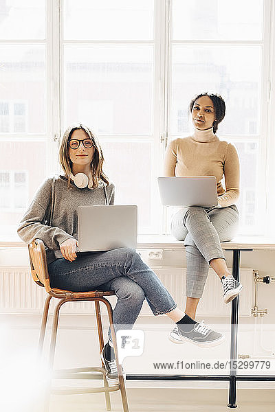 Portrait of female computer programmers with laptops sitting at desk in office