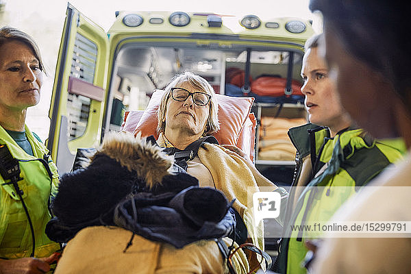 Rettungssanitäter mit reifer Patientin auf Krankenhausbahre gegen Krankenwagen