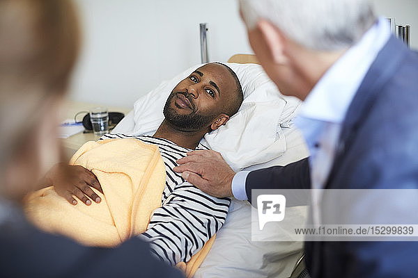 Young man looking at family while lying on bed at hospital