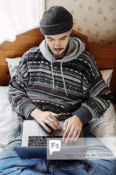 Hochwinkelansicht eines jungen Mannes  der einen Laptop benutzt  während er zu Hause auf dem Bett liegt