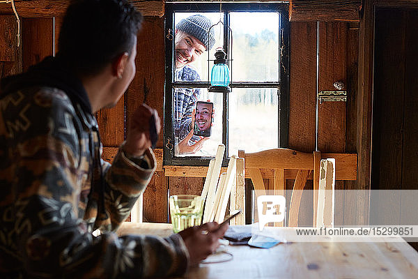 Mann zeigt einem Freund  der in einer Hütte sitzt  ein Foto über ein Smartphone