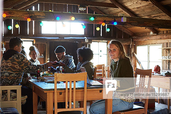 Portrait of young woman using laptop on table while friends enjoying in background at home