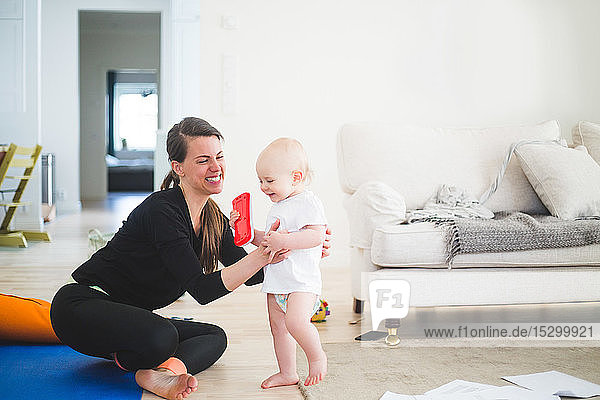Cheerful working mother holding daughter while exercising in living room at home office