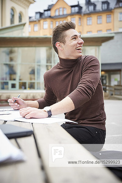 Smiling teenage boy looking over shoulder while sitting at table in schoolyard