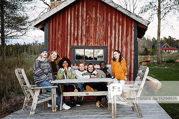 Porträt von lächelnden Freundinnen und Freunden  die bei Sonnenuntergang vor der Hütte sitzen