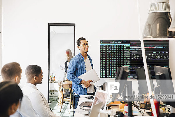 Computer hacker explaining code on television screen to programmers during meeting in creative office