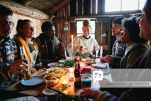 Männliche und weibliche Freunde unterhalten sich beim Essen in der Hütte