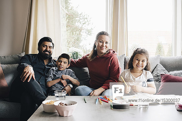 Portrait of smiling family sitting on sofa against window at home