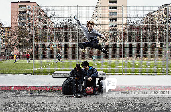Freunde benutzen Mobiltelefon  während ein glücklicher Teenager in der Stadt auf den Bürgersteig springt