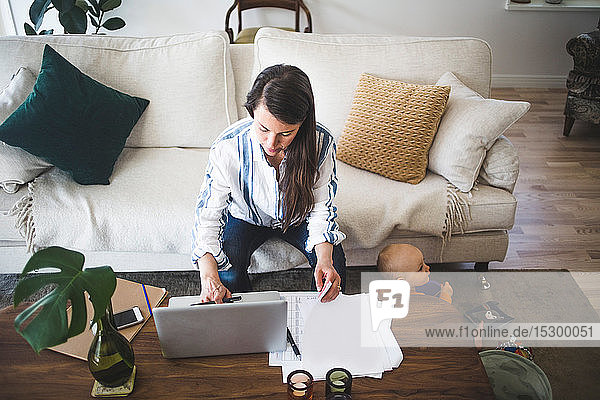 Hochwinkelansicht einer Unternehmerin  die sich auf die Arbeit konzentriert  während ihre Tochter im Heimbüro spielt
