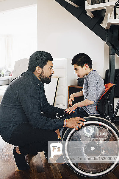Side view of father looking at autistic son sitting on wheelchair at home