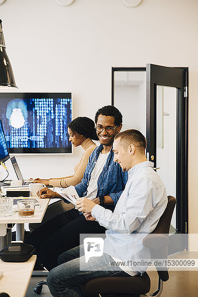 Male programmers discussing while female working in background at creative office