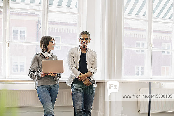 Smiling computer programmers talking while standing by desk in office