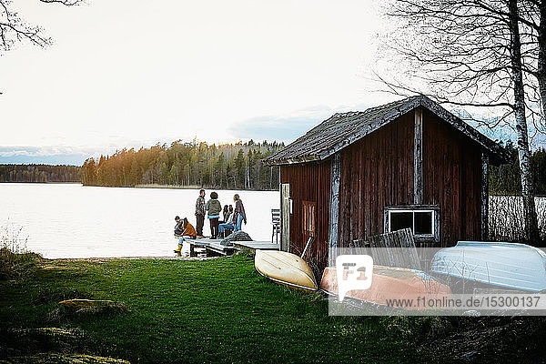 Freunde und Freundinnen unterhalten sich bei Sonnenuntergang vor der Hütte am See