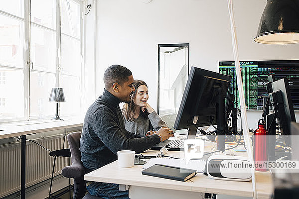 Lächelnde Software-Programmierer diskutieren über Laptop auf Schreibtisch im Büro