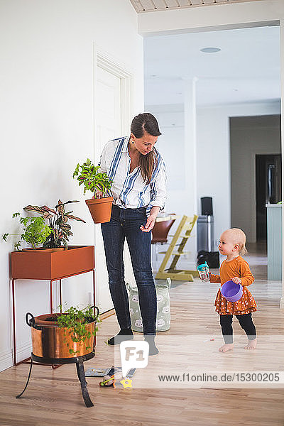 Mutter hält Topfpflanze  während sie die Tochter auf dem Hartholzboden im Wohnzimmer betrachtet