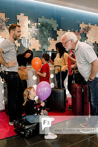 Grandfather talking to girl holding balloon while sitting on suitcase in hotel