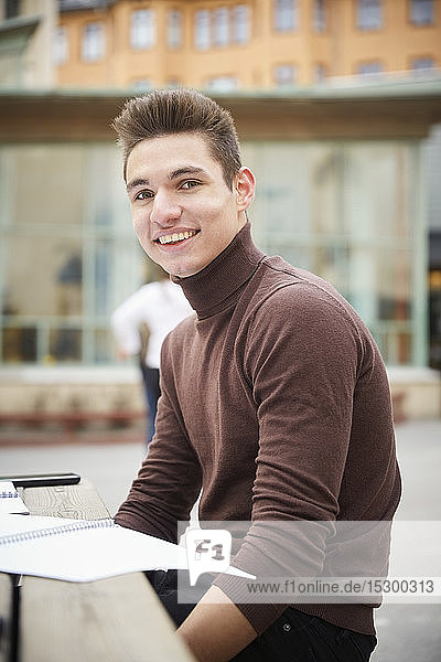 Porträt eines lächelnden Teenagers  der am Tisch auf dem Schulhof sitzt