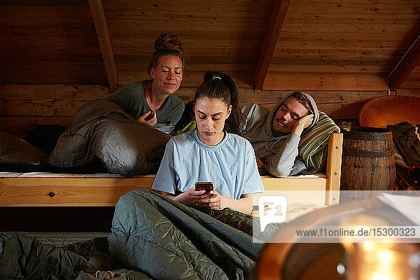 Freunde schauen Frauen an  die ein Smartphone benutzen  während sie sich auf einem Bett in einem Ferienhaus entspannen