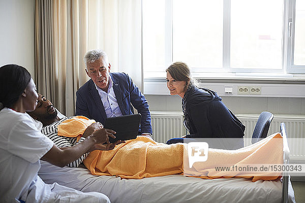 Ärztin zeigt digitales Tablett einem Patienten mit Familie auf der Krankenhausstation