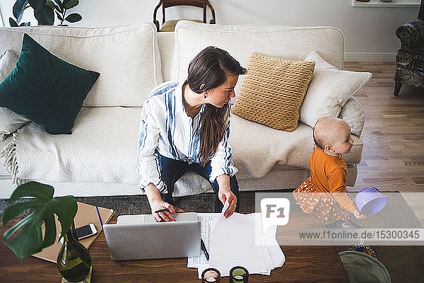 Schrägaufnahme einer Mutter  die ihre spielende Tochter anruft  während sie im Wohnzimmer im Heimbüro arbeitet