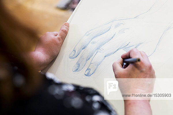 Hochwinkel-Nahaufnahme einer Künstlerin  die eine menschliche Hand zeichnet.