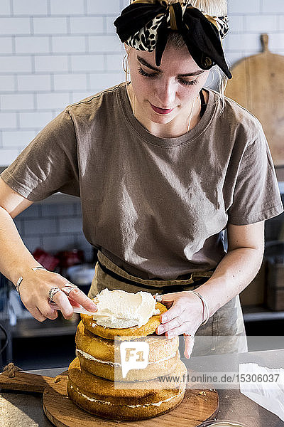 Ein Koch  der in einer Großküche arbeitet und einen Biskuitkuchen mit frischer Sahne zusammensetzt.