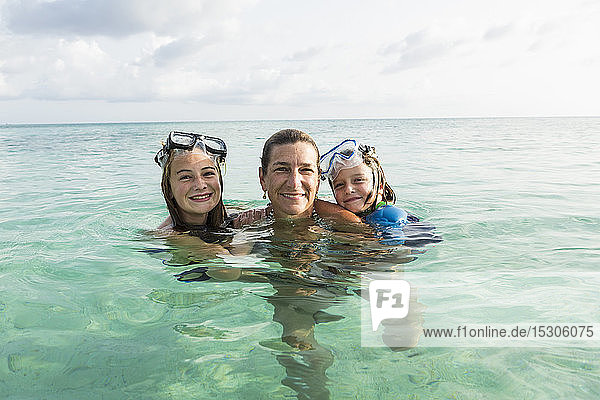 Adult woman standing in ocean water at sunset with her children