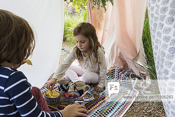 Young boy and girl playing in outdoor improvised tent
