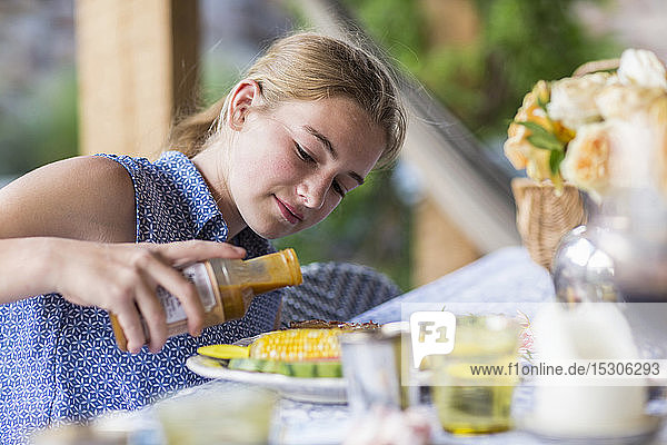 A teenage girl pouring BBQ sauce on ribs and corn