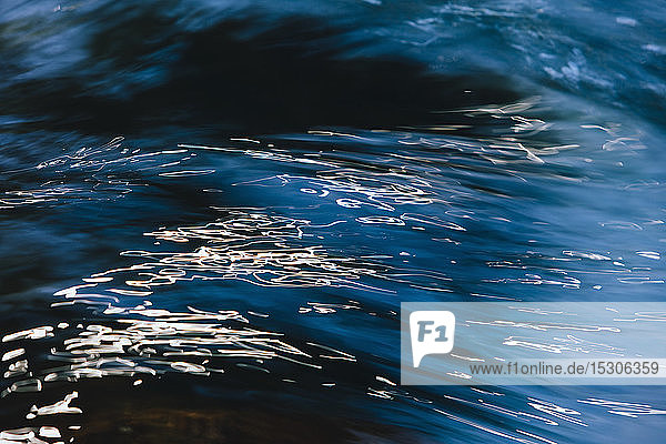Abstrakte Nahaufnahme von fließendem Flusswasser mit Lichtreflexionen an der Oberfläche.