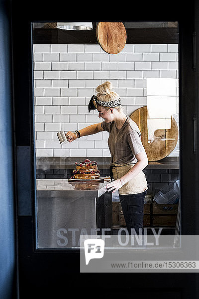 Blick durch eine Tür mit der Aufschrift Staff Only auf einen Koch  der in einer Großküche arbeitet und Puderzucker über einen Schichtkuchen mit frischem Obst streut.