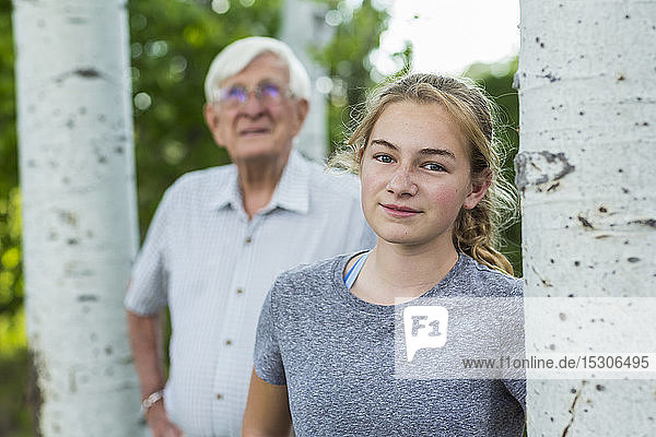 Ein Großvater und seine Enkelin zusammen unter Bäumen in einem Garten.