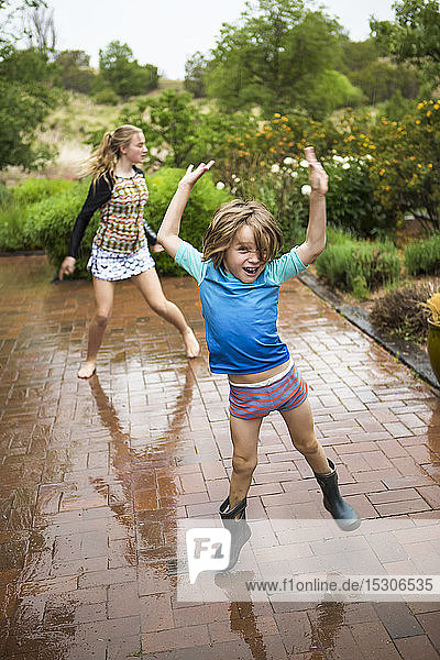 5 Jahre alter Junge und seine 13 Jahre alte Schwester tanzen im Regen.