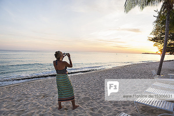 Erwachsene Frau fotografiert mit einem Smartphone am Strand