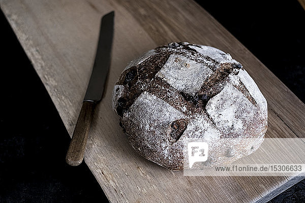 Ein Laib frisch gebackenes Schwarzbrot mit einer dicken Kruste auf einem Brotbrett.