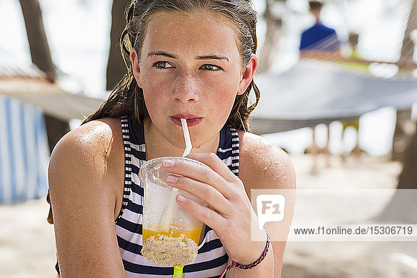 A teenage girl resting in hammock sipping fruit drink