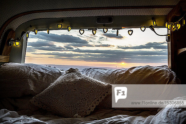 Wohnmobil mit Kissen und Lichterkette  Blick durch die Heckscheibe bei Sonnenuntergang.