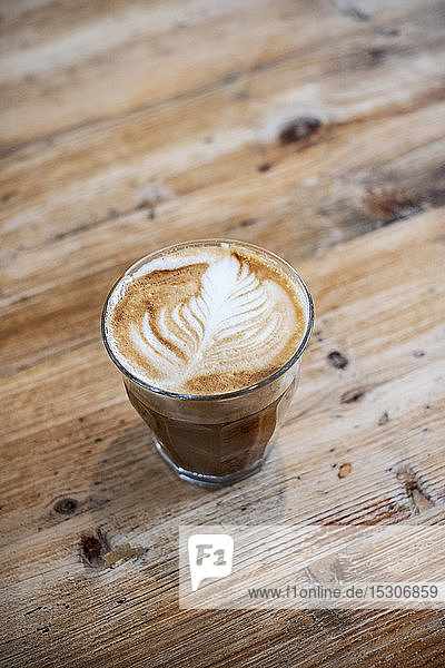 Hochwinkel-Nahaufnahme eines Cafe Latte-Glases auf einem Holztisch.